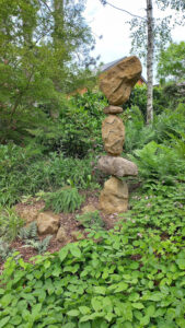 Sculpture de rocailleur surplombant des fougères de collection et des épimédiums parmi fougères sauvages et hostas .Jardin de sous-bois - jardin grelinette et pinceaux